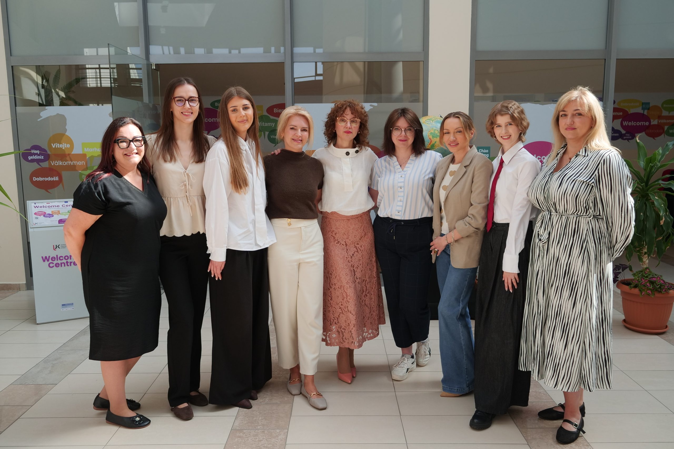 Representatives of UJK's internationalisation division, including the Vice-Rector for Internationalisation, Welcome Centre staff, Erasmus participants and accounting colleagues, pose together in front of the Welcome Centre display.